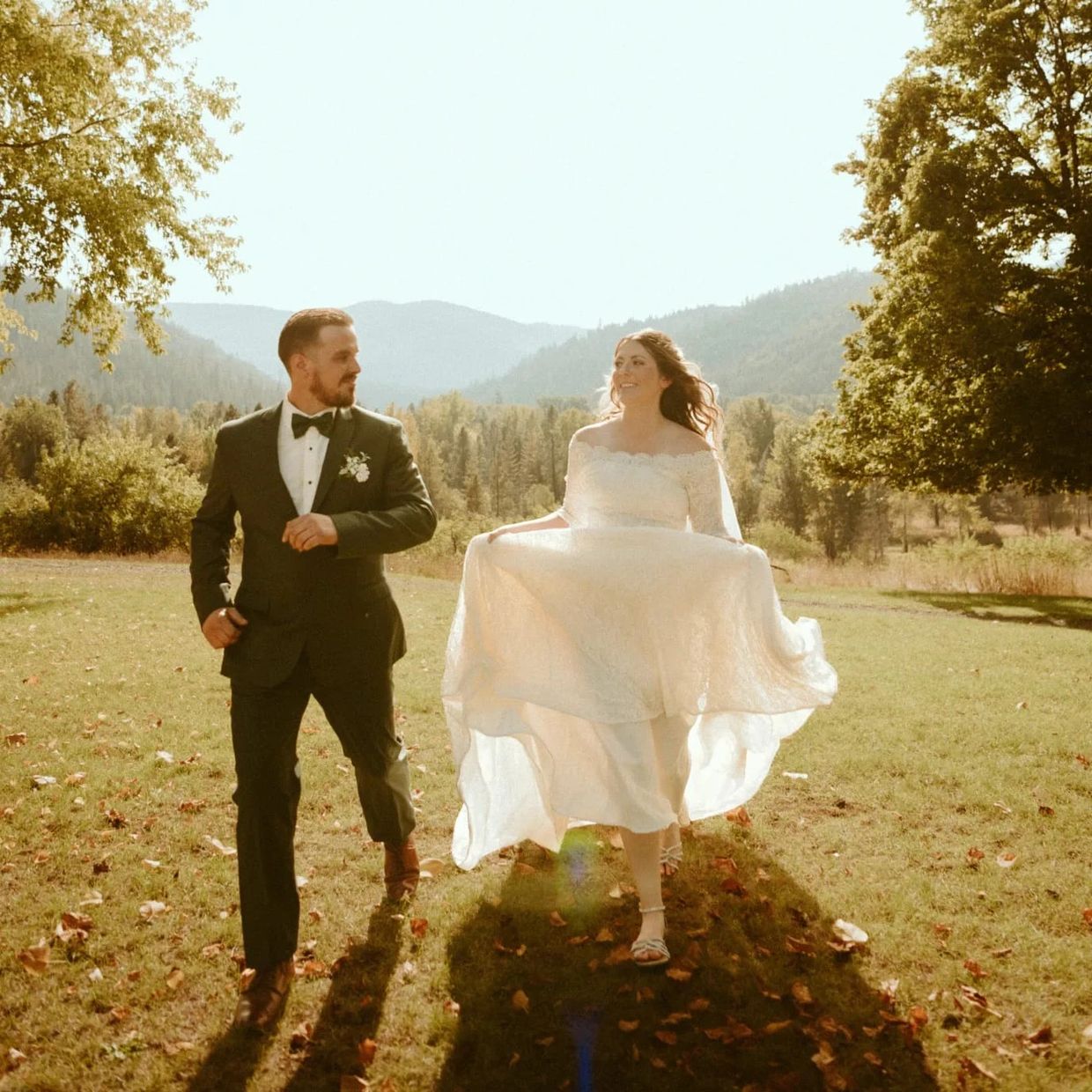 Groom and bride walking outside near trees with mountains in the background in northern Idaho.