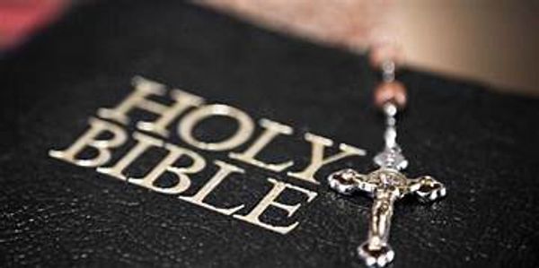 Close-up of a Holy Bible with a silver crucifix on top.