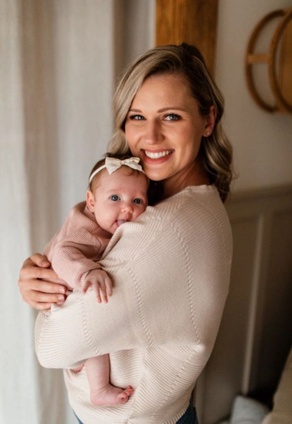 Smiling woman holding a baby wearing a bow headband.