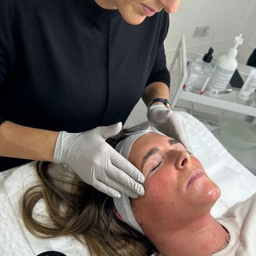 A skincare professional performs a facial treatment on a relaxed woman.