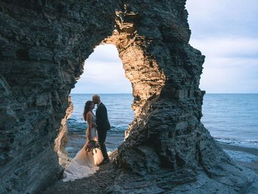 Nova Scotia elopement with bride and groom standing in a rocky arch on a beach.