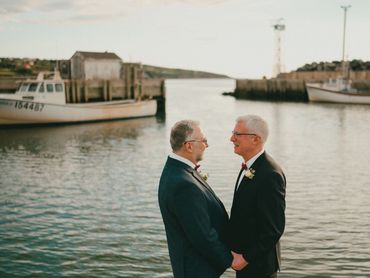 Nova Scotia elopement with two grooms standing in front of lobster boats in a harbour.
