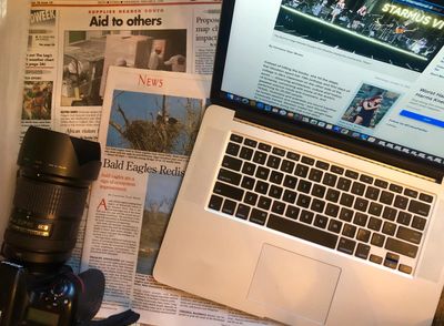 Camera sits atop two newspapers with bylines, and an open laptop is open to today's multimedia story