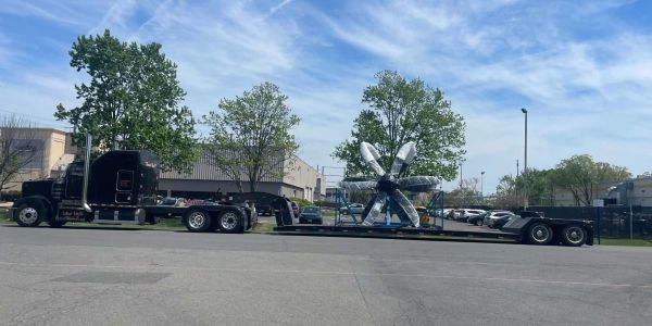 Large truck transporting a huge propeller outdoors.