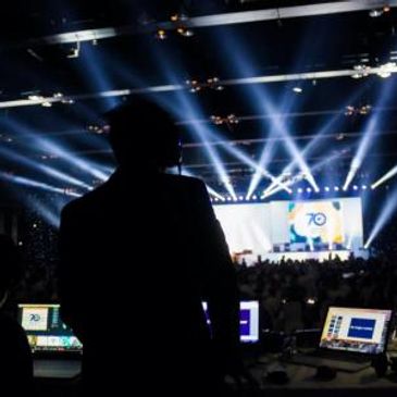 Silhouette of a person at a control desk with stage lights and crowd.