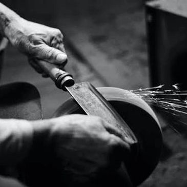 Hands sharpening a knife on a grinding wheel with sparks flying.