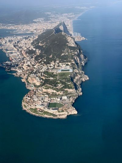 Aerial view of a coastal city with a prominent rocky hill extending into the sea.