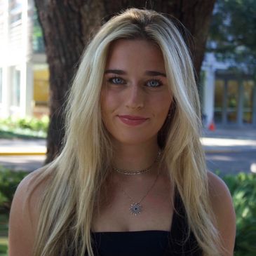 Young woman with long blonde hair and blue eyes smiling outdoors.
