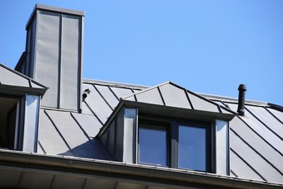 Modern metal rooftop with windows and chimney under clear blue sky.