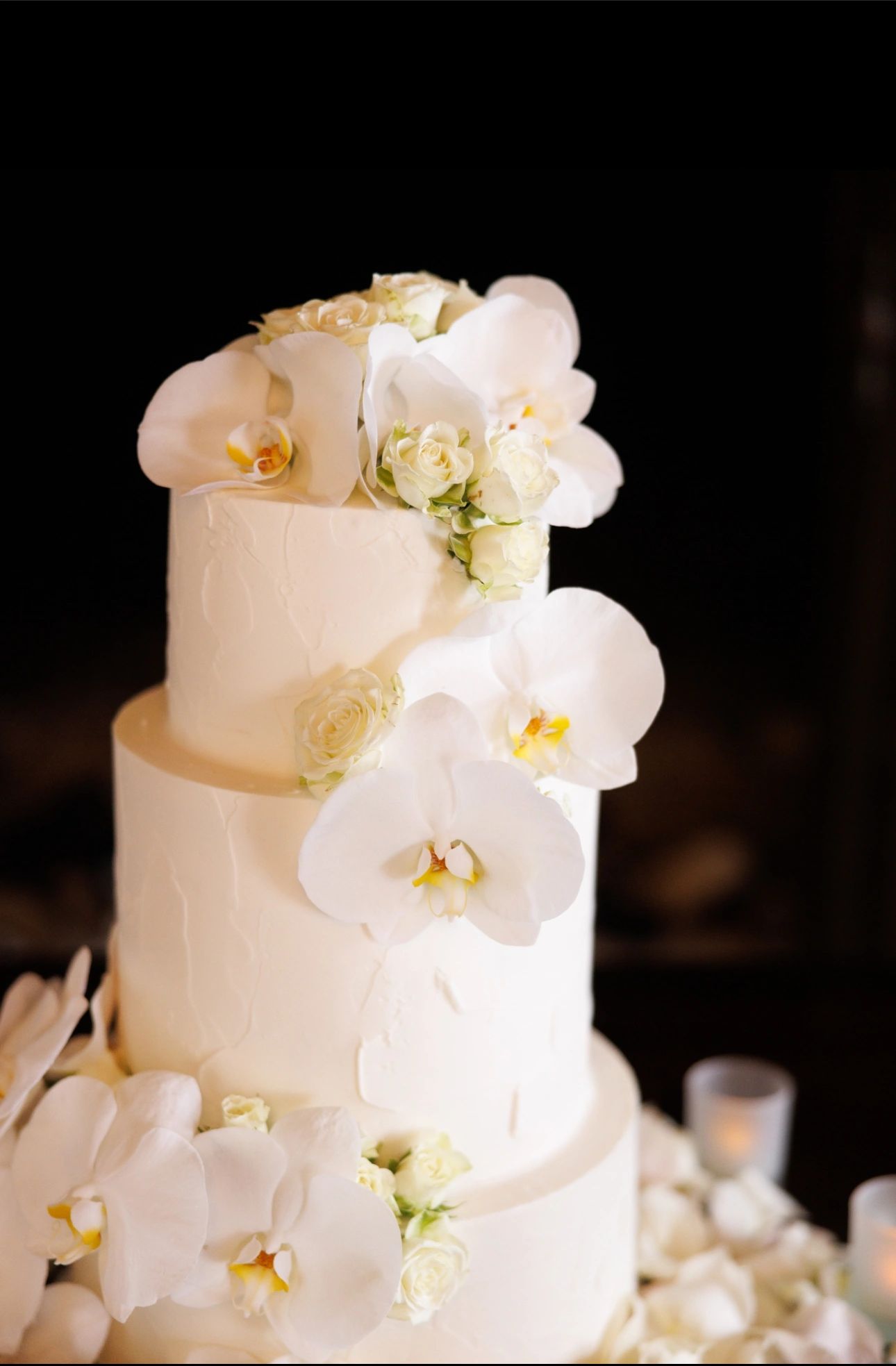 Elegant white wedding cake adorned with white orchids and roses.