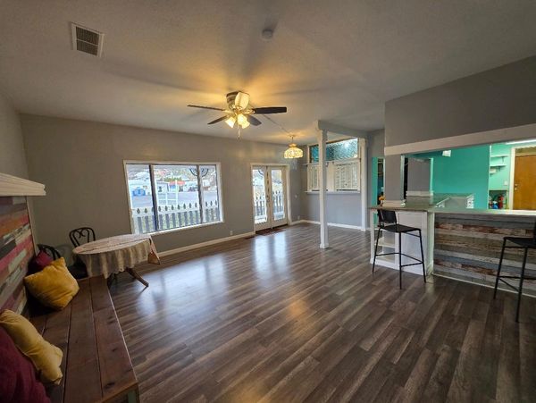 Spacious living room with wood floors, ceiling fan, and natural light from large windows.