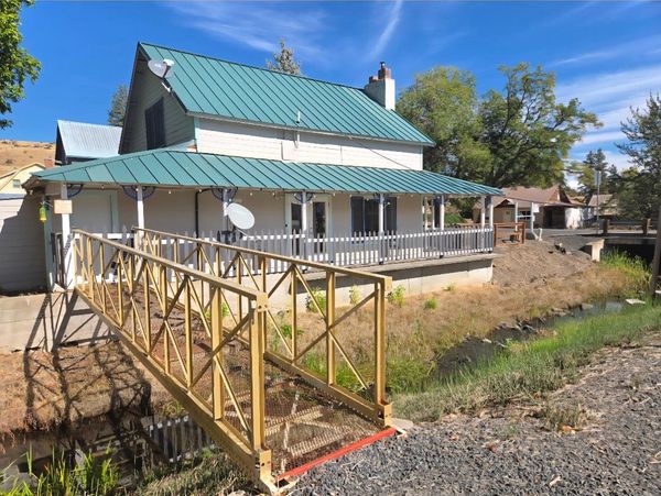 House with green metal roof and small bridge over creek.