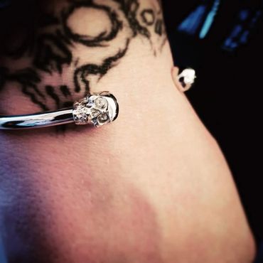 Close-up of a silver bracelet with skull design on a tattooed wrist.