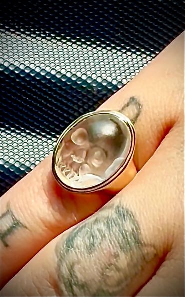 Close-up of a skull ring on a tattooed finger.