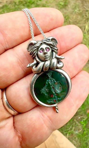 Silver Medusa pendant with pink eyes and a green carved gem depicting a warrior.