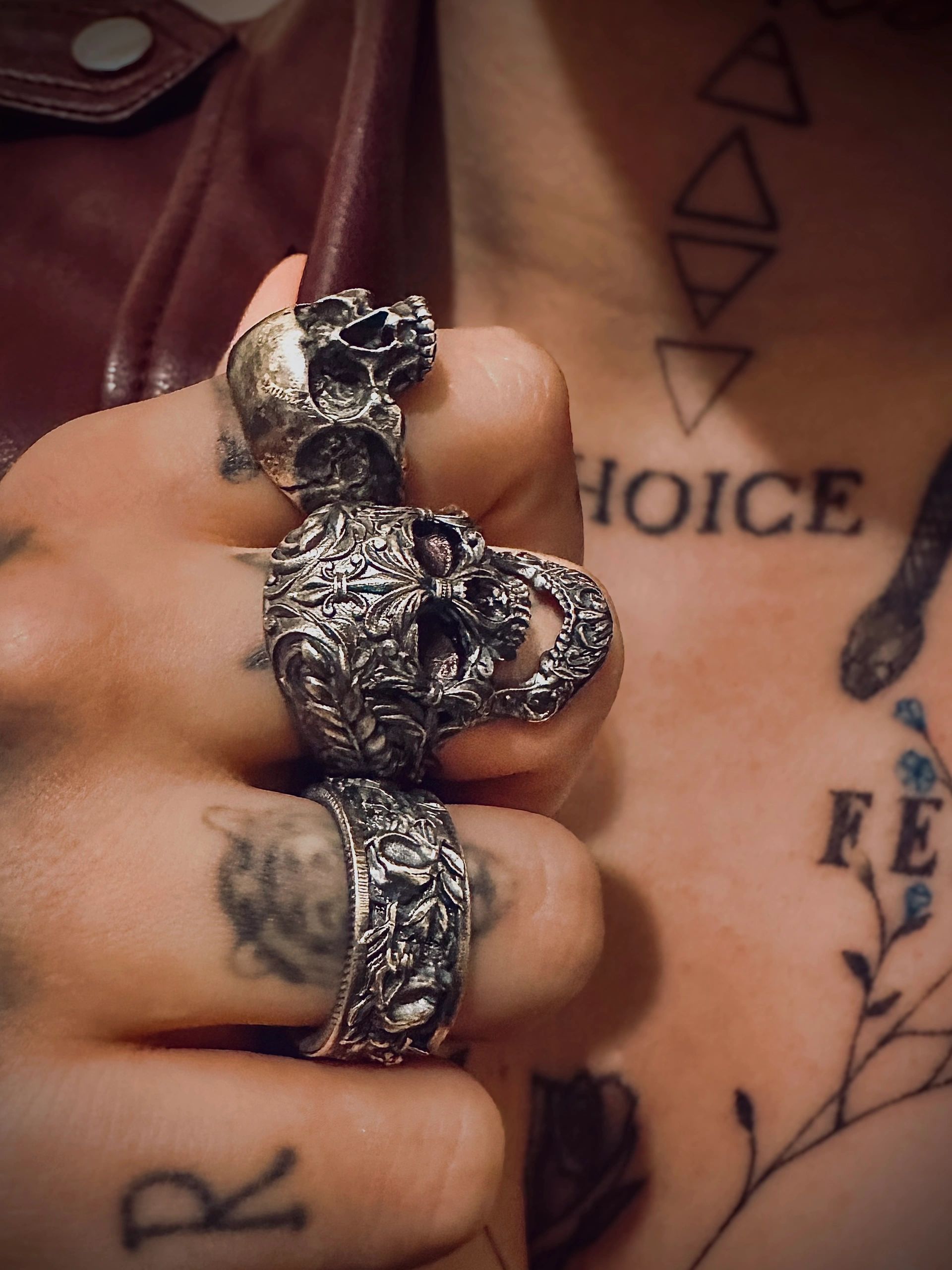 Close-up of a hand wearing ornate skull rings with visible tattoos in the background.