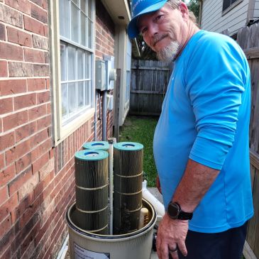 Man in blue shirt inspecting large cylindrical filters outside a house.