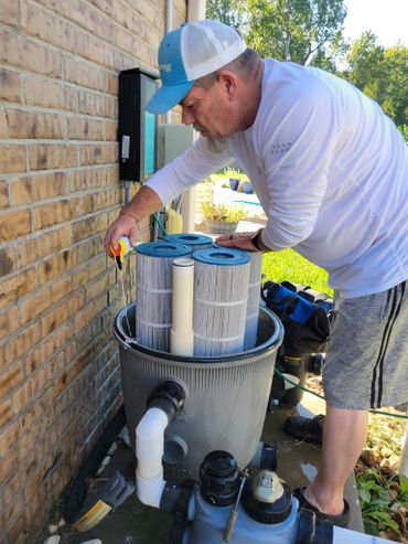 Man working on a pool filter system outdoors near a brick wall.