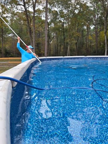 Man cleaning an outdoor above-ground pool with a pole skimmer.