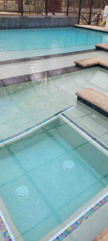 A clean swimming pool with a shallow lounging area and handicap ramp and mosaic tile accents.