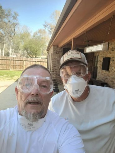Two men wearing safety goggles and masks outdoors near a house getting ready to acid wash a pool.