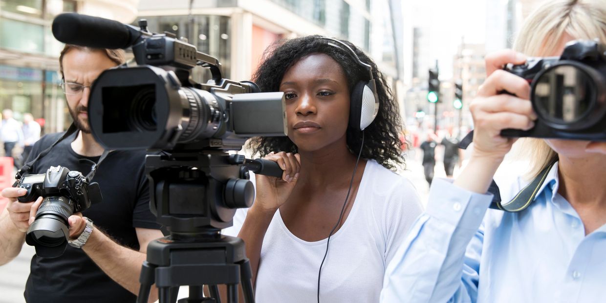 Three photographers and videographers capturing moments with cameras and a video camera outdoors.
