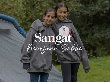 Two girls in matching hoodies smiling outdoors near a tent.
