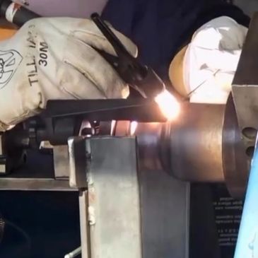 Close-up of a gloved hand welding a metal pipe with a bright flame.