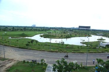 A scenic park with a water body surrounded by greenery and a road with motorcyclists.