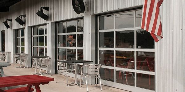 Outdoor seating area with metal tables and chairs beside a building with large windows and an American flag.