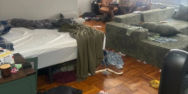 A cluttered bedroom with an unmade bed and scattered clothes on the floor.