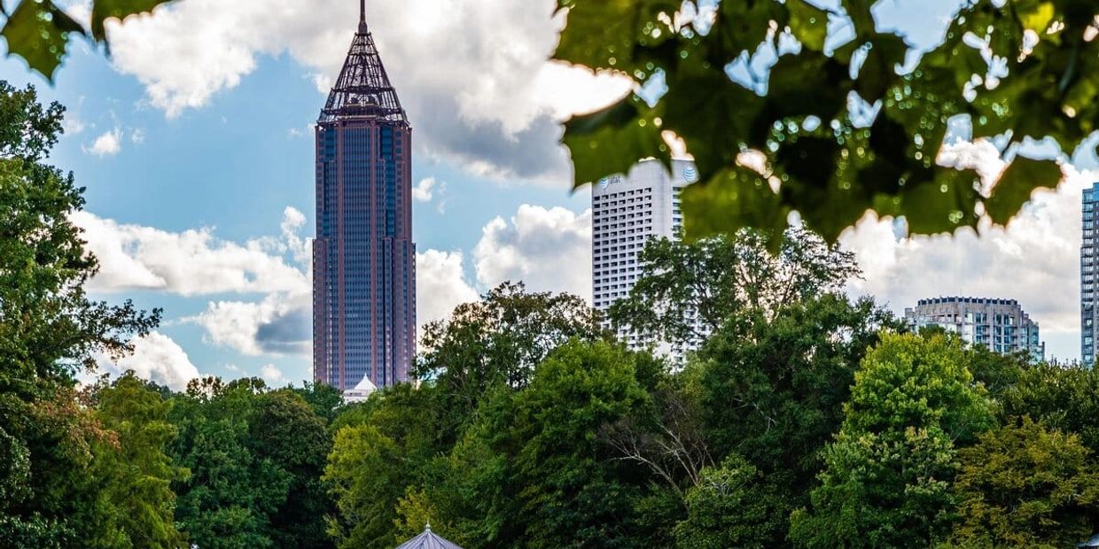 Tall skyscraper rising above green trees under a blue sky with clouds.