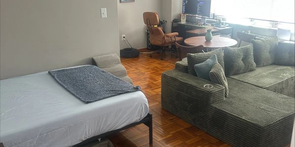 Cozy room with a bed, striped sofa, and workspace by the window.