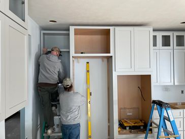 Two workers installing kitchen cabinets and shelves during home renovation.