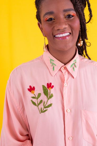 mulher negra sorrindo com camisa bordada