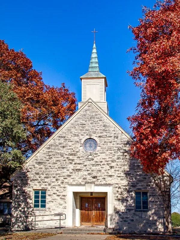 Stone church with wooden doors and autumn foliage.