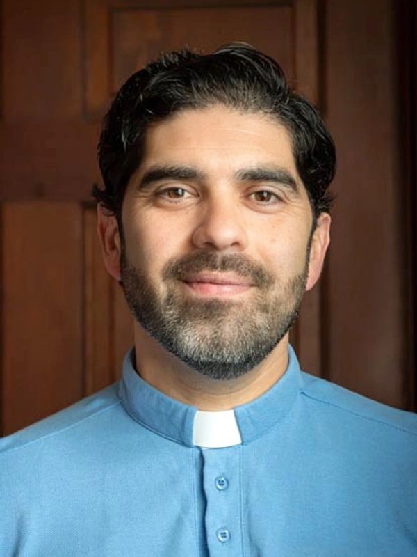 Smiling man in a blue clerical collar shirt.