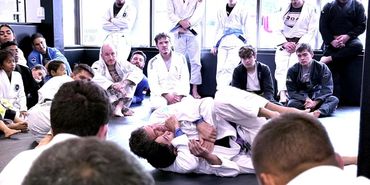 Brazilian Jiu-Jitsu class with students watching a grappling demonstration.