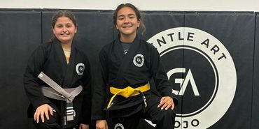 Two young martial artists kneeling in black gis with colored belts.