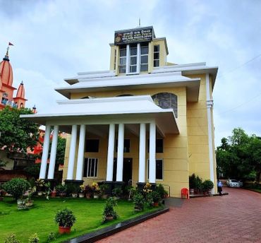 A beige building with white columns and a lush green garden in front.
