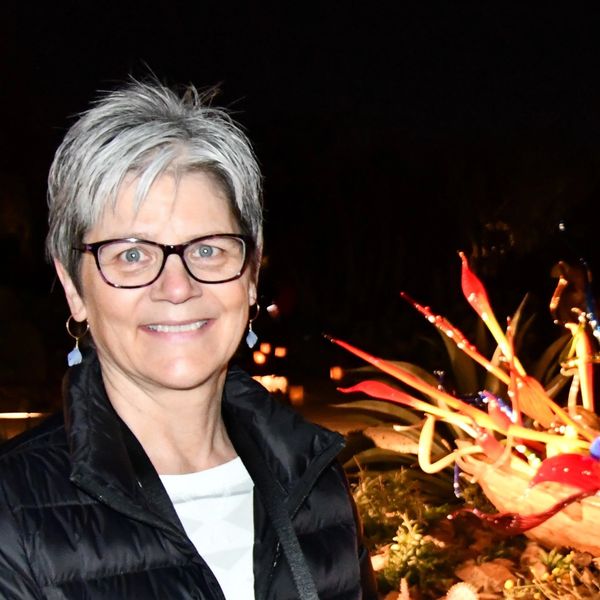 Smiling woman with glasses and short gray hair in a black jacket at night.