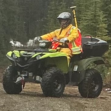 Person in safety gear riding an ATV in a forested area.