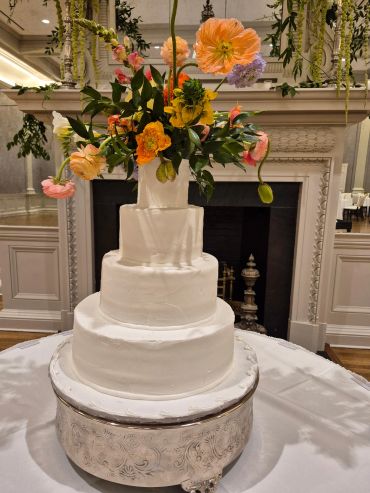 Tall white wedding cake with colorful flowers on top.