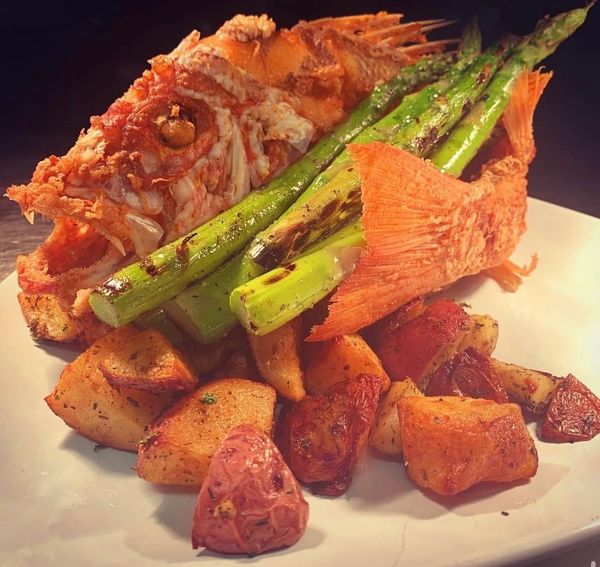 Grilled whole fish served with asparagus and roasted potatoes.