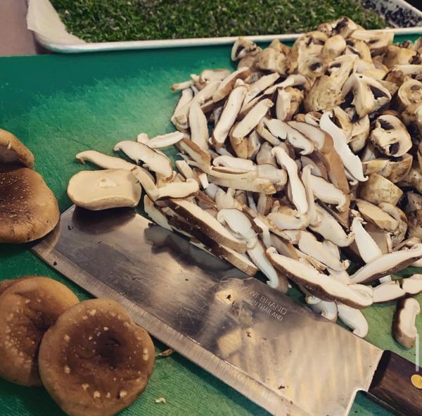 Sliced mushrooms on a green cutting board with a large knife.