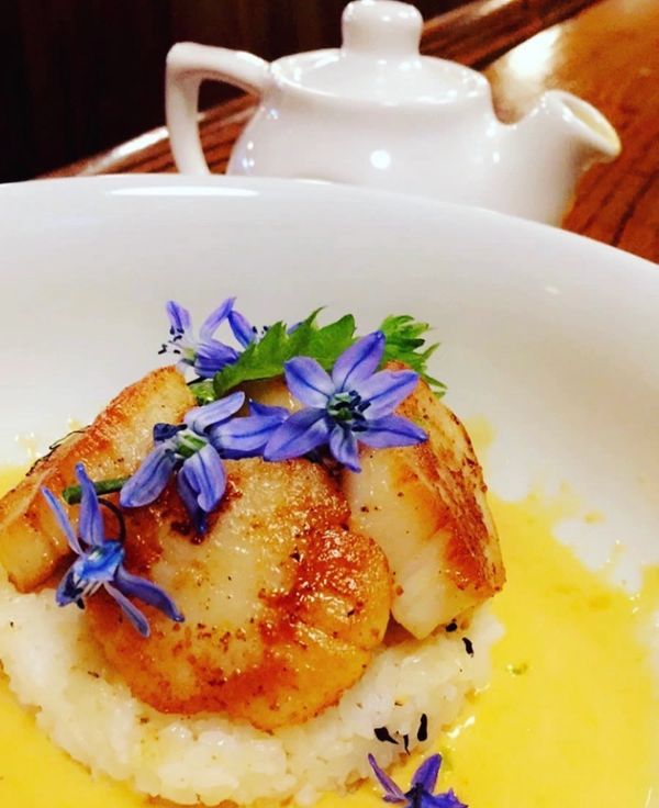 Seared scallops on creamy risotto garnished with blue edible flowers.