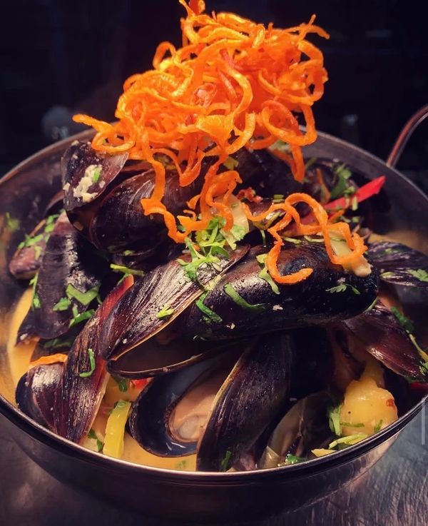 A bowl of mussels garnished with herbs and crispy fried carrot strips.