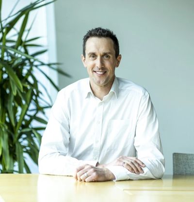 Man in white shirt sitting at a table, smiling.