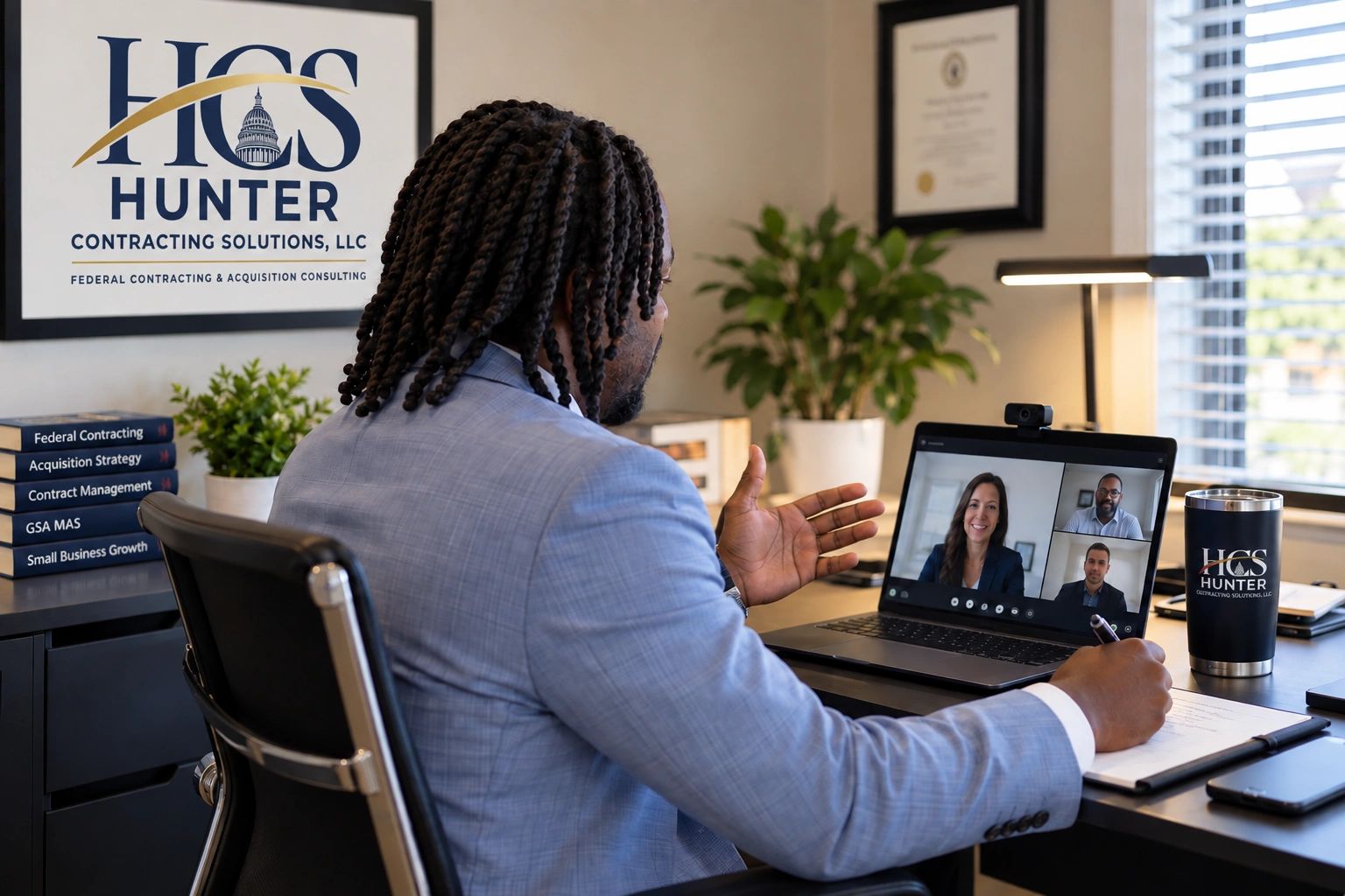 Man in a suit participating in a video conference at office desk.