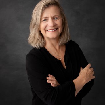 Femme souriante en pull noir avec les bras croisés.